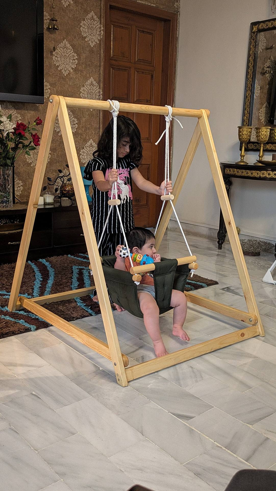 Children playing on a wooden swing set indoors.
