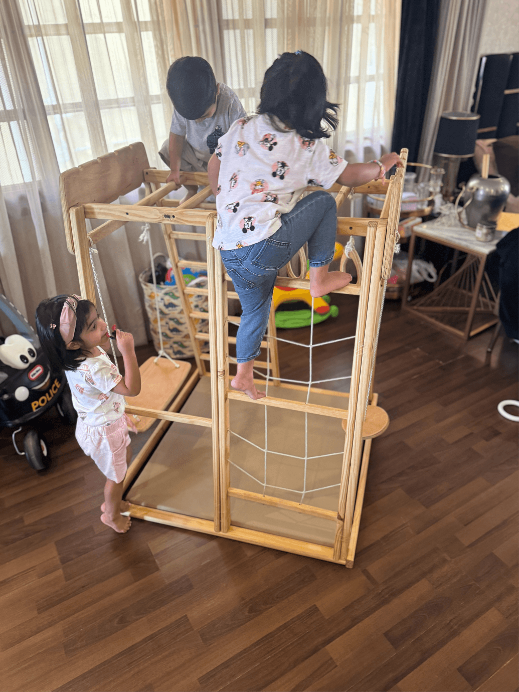 Children playing on a wooden jungle gym in a home setting.