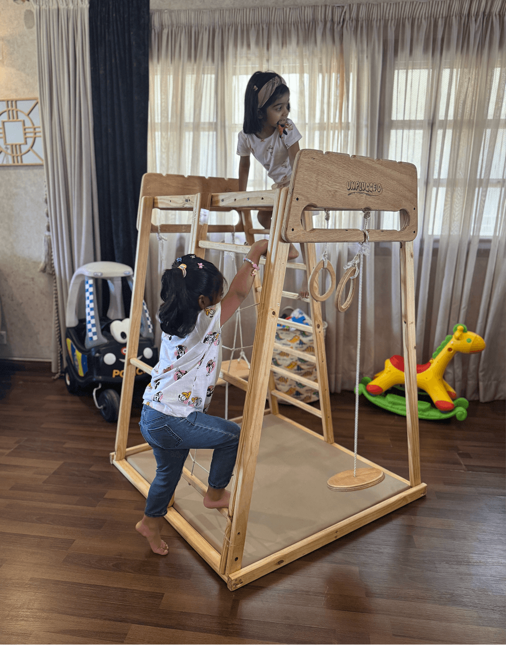 Children playing on a wooden jungle gym in a room with toys around