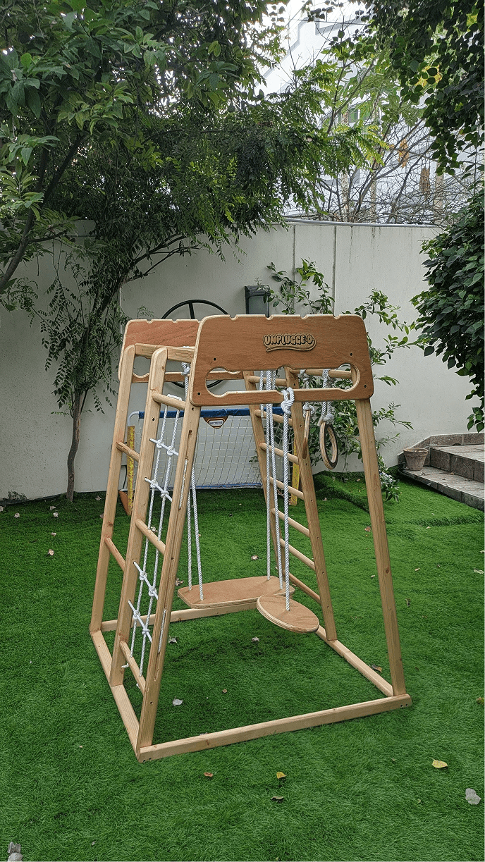A wooden jungle gym in a room featuring swing, monkey bar, rope ladder