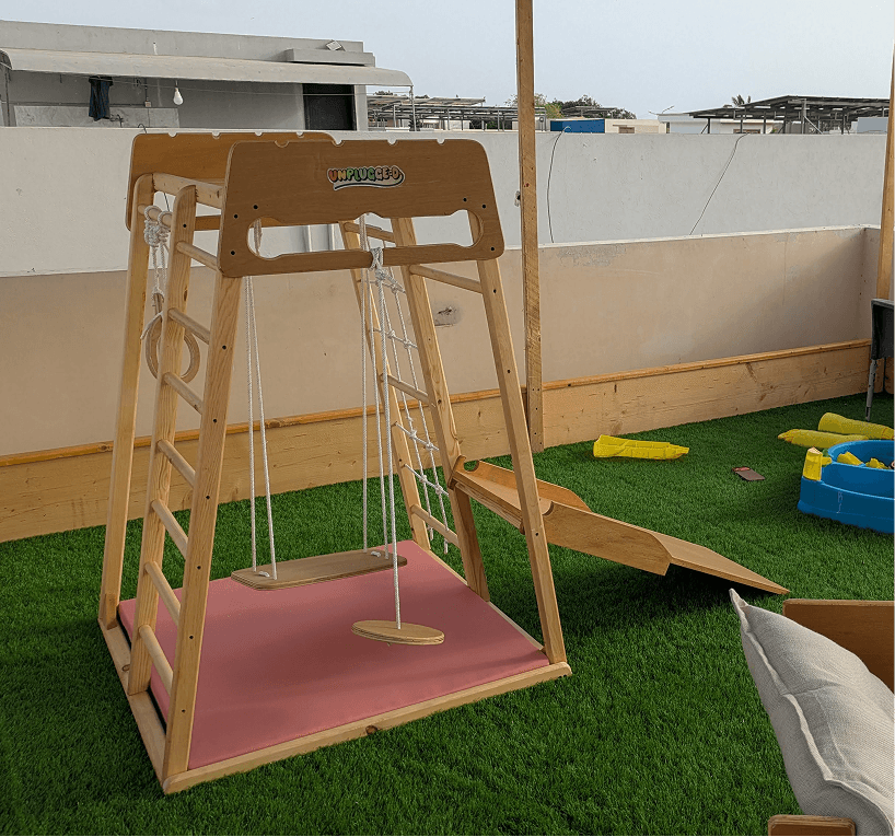 Children's wooden jungle gym with swing and slide on a grassy area.