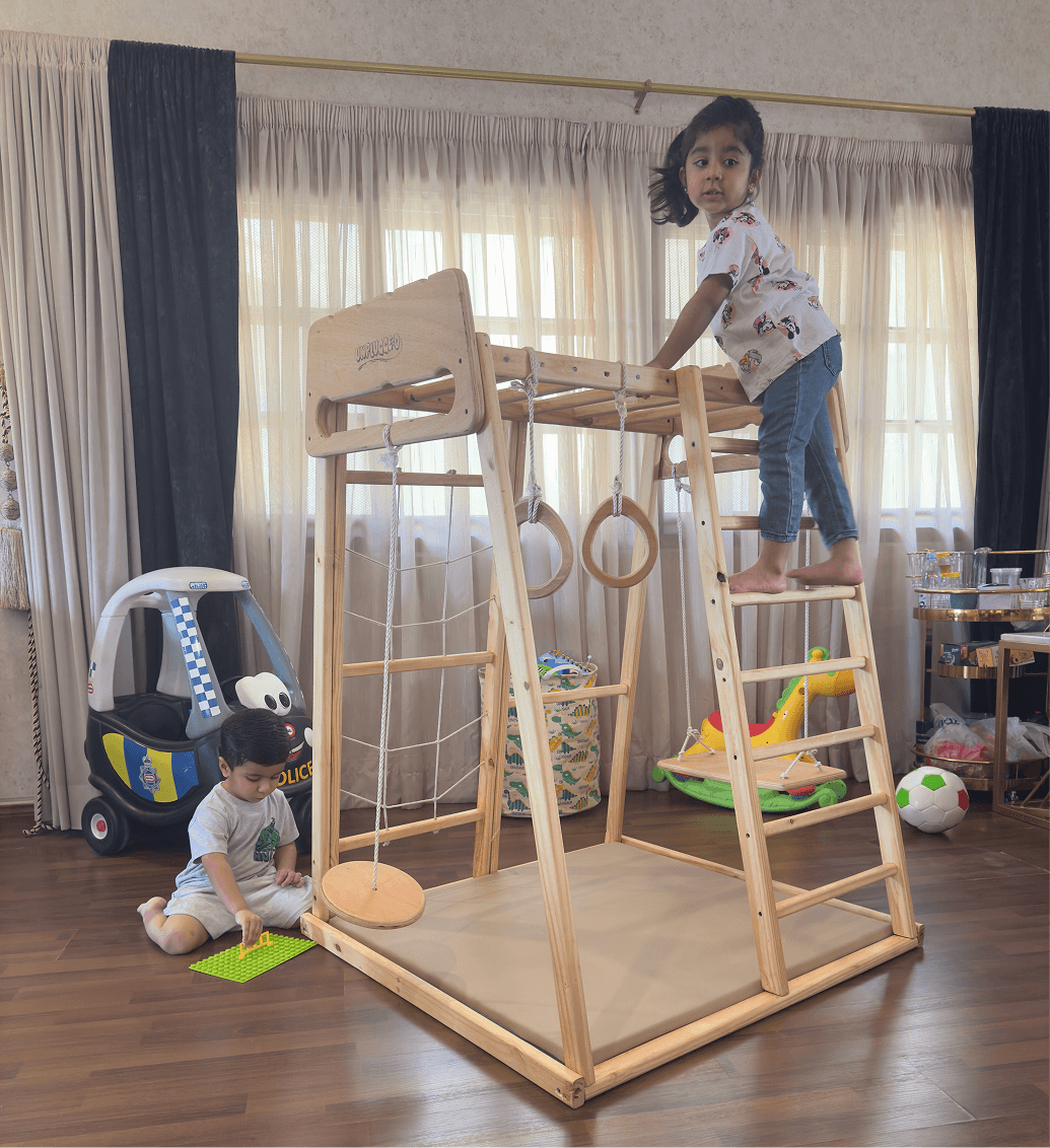 Children playing on a wooden jungle gym in a room with toys around