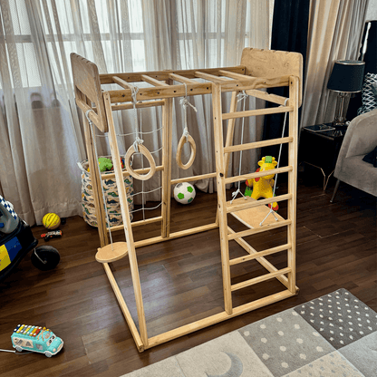 Wooden jungle gym with swing, gymnastic rings, ladder and monkey bar in a room with toys and furniture.